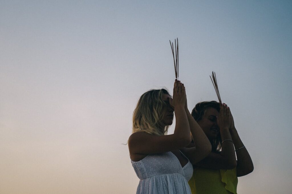 Two women meditating with incense at sunset, creating a serene and calming atmosphere.
